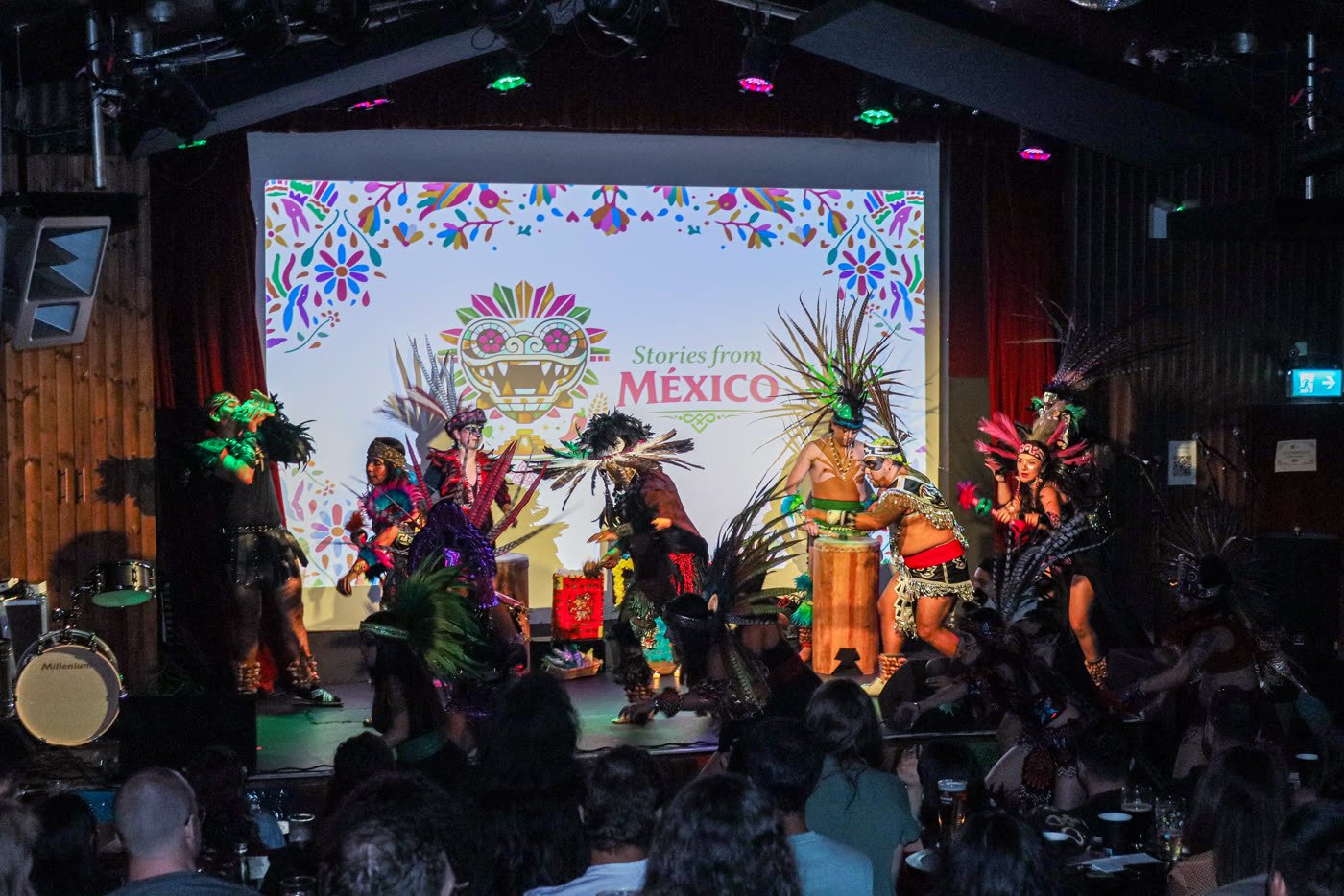 Calpulli Mictlán performing Aztec dance on stage with the Stories From México logo