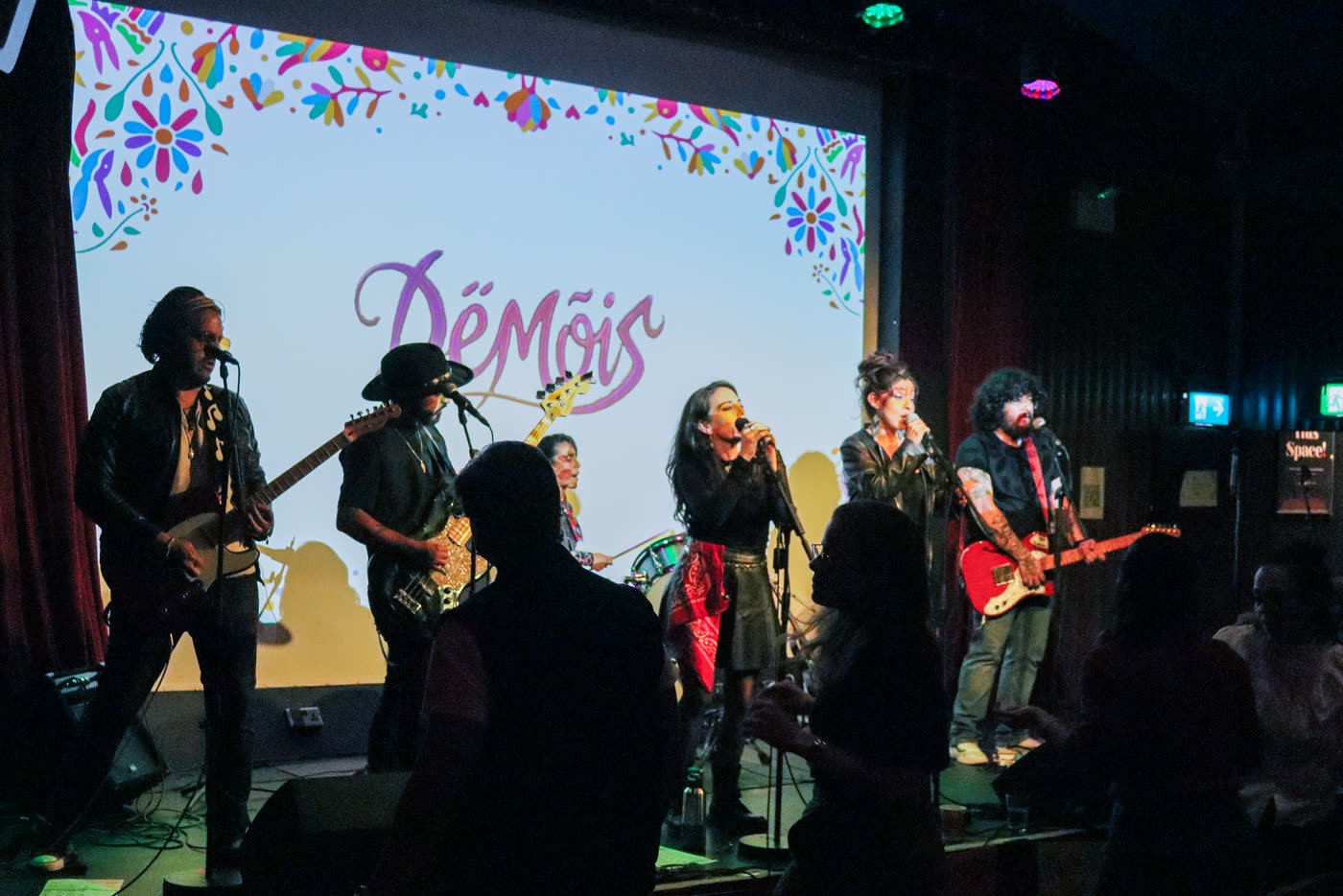 The full Dëmöis band performing with their logo on screen